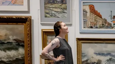 A person stands in front of various pieces of artwork